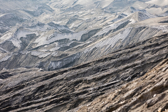 View of rugged, ash-covered terrain under a hazy sky, revealing the volcanic landscape's raw beauty and desolation, Mount Bromo Volcano, East Java, Indonesia.