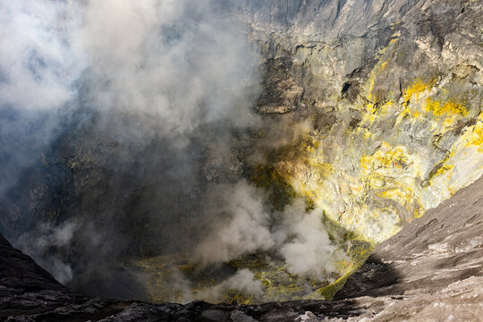 View of a smoking volcano crater with yellow sulfur deposits clinging to the rugged walls, shrouded in ethereal mist, Mount Bromo, East Java, Indonesia.