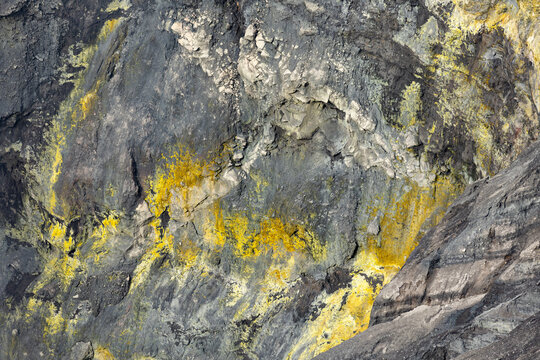 View of volcanic rock face streaked with vibrant yellow sulfur deposits creating a stark contrast against the dark stone, Mount Bromo, East Java, Indonesia.