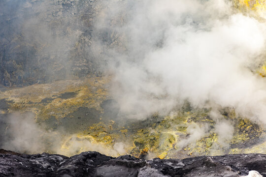 View of volcanic terrain with sulfur deposits and billowing white smoke rising from the crater, Mount Bromo Volcano, East Java, Indonesia.
