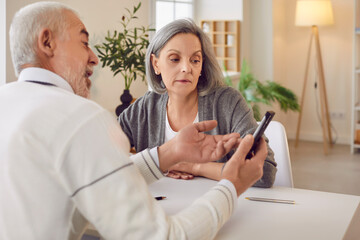 Elderly couple spending leisure time together online using a phone at home. Positive and happy...