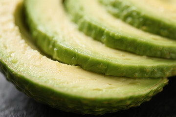 A close-up of avocado slices arranged in a subtle overlap, showcasing the creamy pale green flesh fading into a darker edge at the skin. The texture appears soft and smooth, suggesting ideal ripeness.