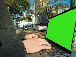 Student working on laptop with green screen in urban park setting