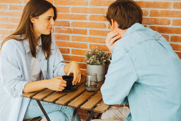 Young couple or friends Eva and Nil chatting happily at table – casual meeting, friendly...
