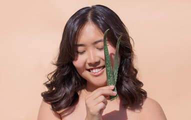 Young woman with dark hair joyfully holding fresh aloe vera leaf, showcasing natural beauty and...