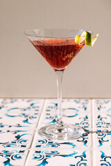 Close-up of a martini glass on a table with patterned tiles. An elegant goblet with an alcoholic sparkling drink decorated with lime zest. Tasty berry cocktail.