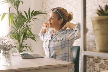 Woman smiles and stretches at the desk in her room or office in front of the laptop. Overwork....