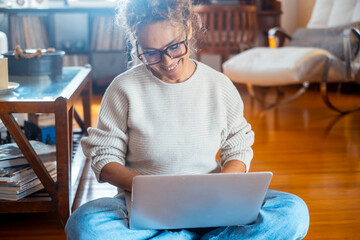 Curly-haired woman in her 40s using a laptop at home with varied expressions. Remote work, digital...