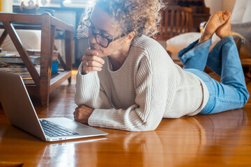 Curly-haired woman in her 40s using a laptop at home with varied expressions. Remote work, digital...