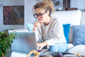 Curly-haired woman in her 40s using a laptop at home with varied expressions. Remote work, digital...