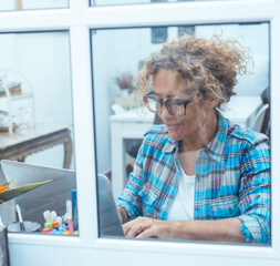 Curly-haired woman in her 40s using a laptop at home with varied expressions. Remote work, digital...