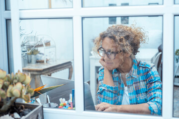 Curly-haired woman in her 40s using a laptop at home with varied expressions. Remote work, digital...