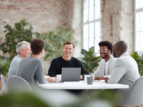 Diverse team collaborating around a table, sharing ideas in a bright, modern office. Illustrates teamwork, innovation, and a positive work environment. Perfect for corporate or business concepts.