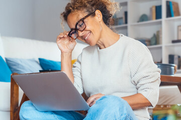 Smiling curly-haired woman in her 40s working on a laptop at home. Remote work, online business,...