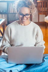Smiling curly-haired woman in her 40s working on a laptop at home. Remote work, online business,...