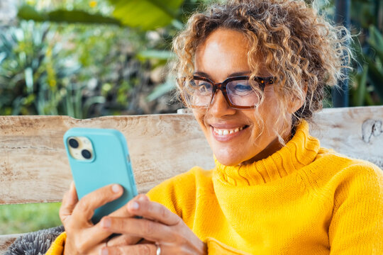 Curly-haired woman in her 40s using smartphone outdoors. Modern lifestyle with technology, chatting, calling, browsing, installing apps, staying connected and enjoying digital freedom on the go