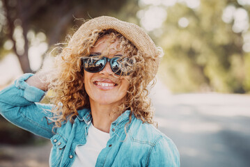 Portrait of wonderful white female model with curly blonde hair expressing energy on a good day in Europe. Beautiful curly woman smiling and walking with trees behind her.