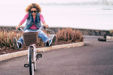 Smiling curly-haired woman in her 40s riding a city bicycle outdoors. Healthy lifestyle,...