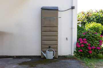 Un réservoir d’eau de pluie rectangulaire est installé contre un mur extérieur, relié à une...