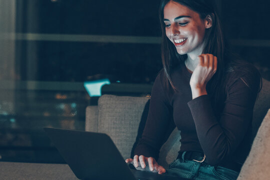 Young woman using laptop at night, smiling and enjoying online life. Late work session, video chat, dating, remote connection, insomnia, smart working, modern lifestyle and digital independence