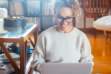 Beautiful curly-haired woman in her 40s wearing glasses, using laptop at home or office. Remote...