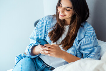 Smiling young woman using smartphone to browse, chat, and connect online. Modern lifestyle with...