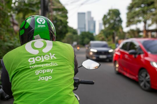 Gojek delivery rider wearing a branded green jacket and helmet.