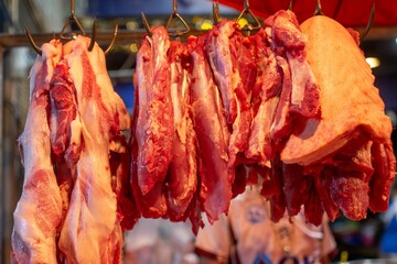 Row of fresh, uncooked meat pieces is hanging from metal hooks.