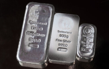 Three silver bars of different weight on a dark background.