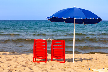 Beach chairs and umbrella on sandy beach facing sea under clear summer sky