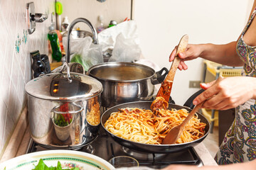 Woman cooking spaghetti with tomato sauce in home kitchen using wooden utensils on stove
