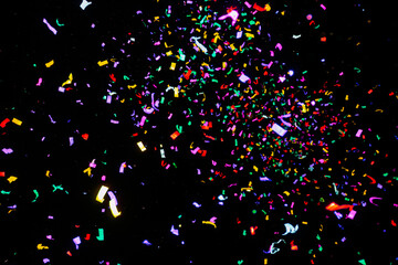 Colorful confetti pieces flying through dark air during night celebration or party event
