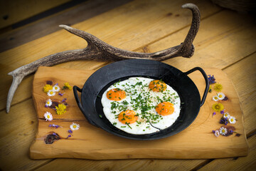 four fried eggs with chive served in a iron pan, on a wood board decorated with flowers