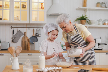 Happy family in kitchen. Grandmother and granddaughter child cook in kitchen together. Grandma teaching kid girl knead dough bake cookies. Household teamwork helping family generations concept