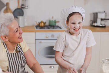 Happy family in kitchen. Grandmother and granddaughter child cook in kitchen together. Grandma teaching kid girl knead dough bake cookies. Household teamwork helping family generations concept