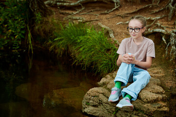 A nine-year-old girl with glasses is relaxing in the forest.