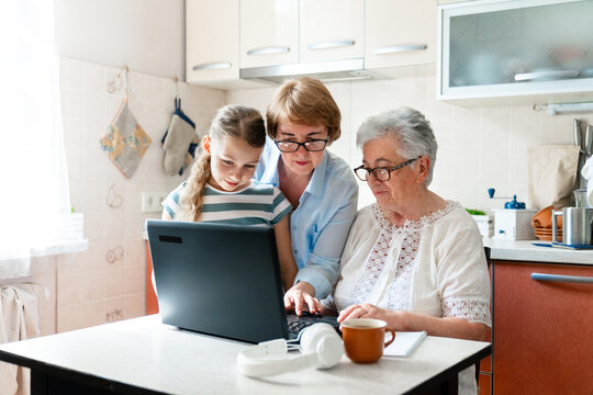 Senior woman learning computer skills with help from multigenerational family, using laptop at home. Digital literacy, education and support. Technology lifestyle, equality of three generations