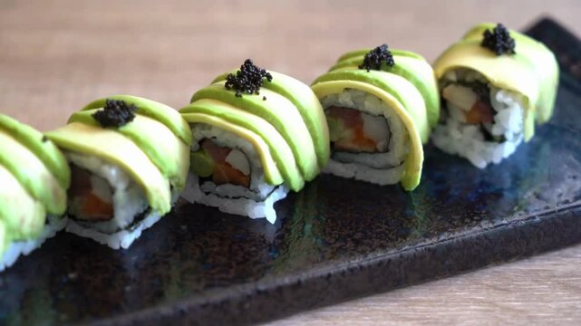 A row of sushi rolls with avocado on a dark plate
