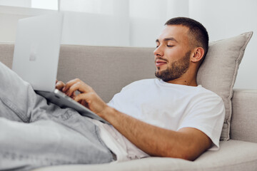 Relaxed man working on a laptop at home, showcasing modern lifestyle and remote work trends in a...