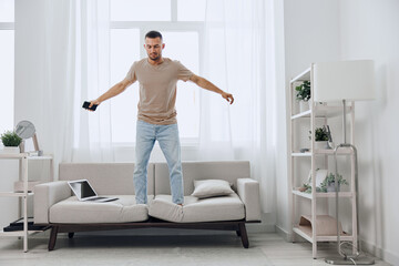 Man balancing on a sofa in a bright room, experiencing tension and uncertainty related to work-life...