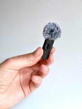 Hand holding a small wireless microphone with a fluffy windscreen, isolated on a white background. Minimalist tech gadget photography.