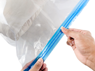 Close up of hands sealing a clear plastic bag with a blue zipper closure containing folded fabric isolated on transparent background