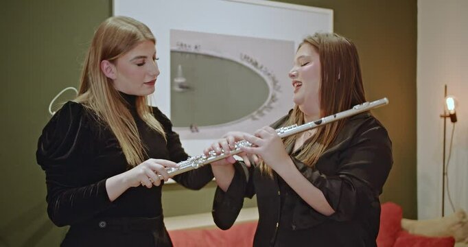 Two women practice playing flute at home, receiving instruction and guidance on proper finger placement and technique.
