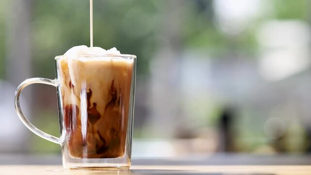 Creamy milk swirls into a glass of iced coffee, creating a mesmerizing marble effect as it blends with the rich, dark brew over ice cubes