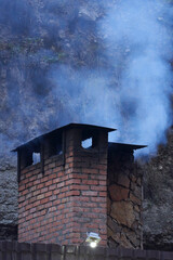 Brick rectangular chimney with billowing white smoke against the backdrop of a steep cliff. Copy space.