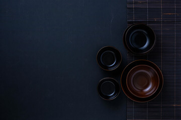 Dark japanese tableware background with bowls and bamboo mat top view for food photography design 100