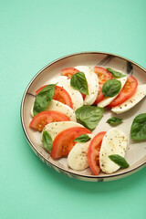 Italian Caprese salad with cherry tomatoes, mozzarella, basil on plate on mint background. Vertical photo