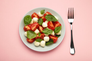 Italian Caprese salad with cherry tomatoes, mozzarella, basil on dark plate on pink background.