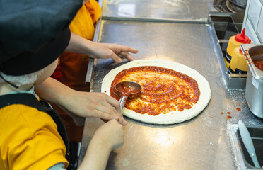 A young boy with short hair spreads tomato sauce on pizza dough.