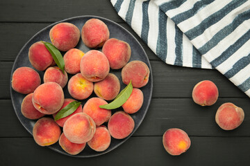 Sweet peaches and leaves on dark plate on black wooden background.